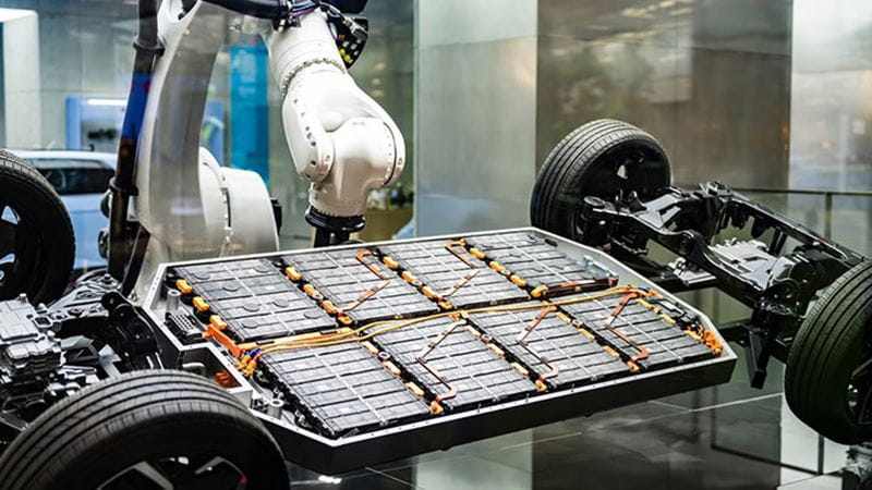 电动汽车底盘上的电池组与自动化机械臂，体现电池技术与制造创新